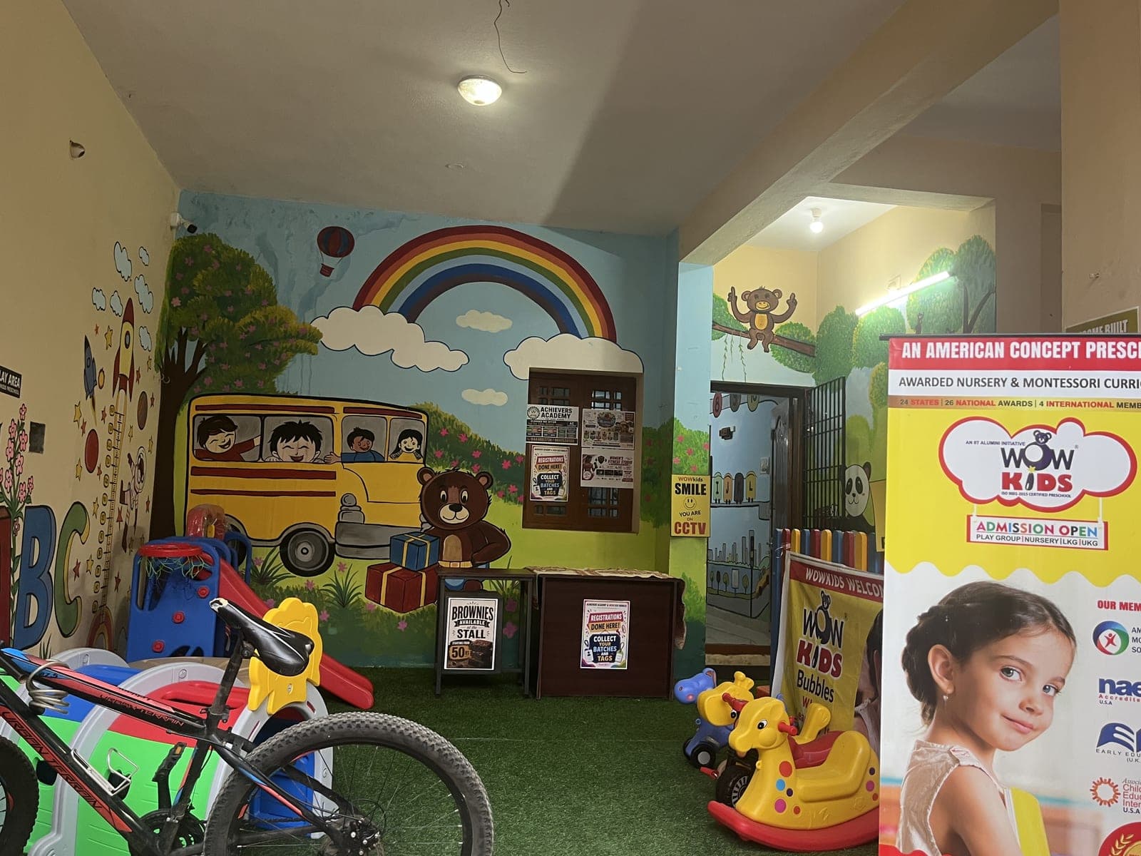 Wow Kids Bubbles indoor play area with a rainbow and school-bus mural, ride-on toys and soft green turf