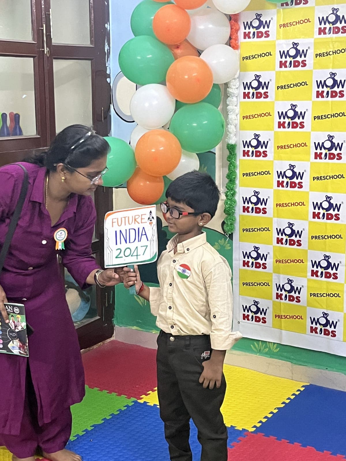 Teacher encouraging a young student holding a “Future India 2047” sign at the Independence Day celebration